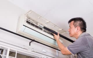 Man cleaning wall-mounted air conditioner with vacuum