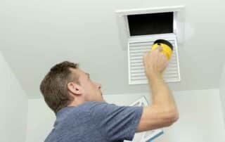 Man inspecting an air duct with a flashlight, highlighting the benefits of regular air duct cleaning for better airflow, efficiency, and indoor air quality.