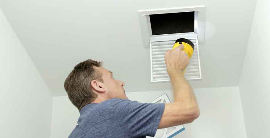 Man inspecting an air duct with a flashlight, highlighting the benefits of regular air duct cleaning for better airflow, efficiency, and indoor air quality.