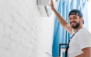 Technician carefully installing an air conditioner on a white brick wall, illustrating that cheap air duct cleaning services may not deliver reliable or high-quality results.