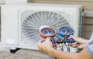 Air repair mechanic using measuring equipment for filling industrial factory air conditioners and checking maintenance outdoor air compressor unit.