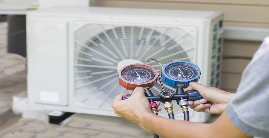Air repair mechanic using measuring equipment for filling industrial factory air conditioners and checking maintenance outdoor air compressor unit.
