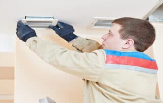 A professional technician wearing gloves installs or adjusts a ceiling air vent cover as part of an air duct cleaning or HVAC maintenance process.