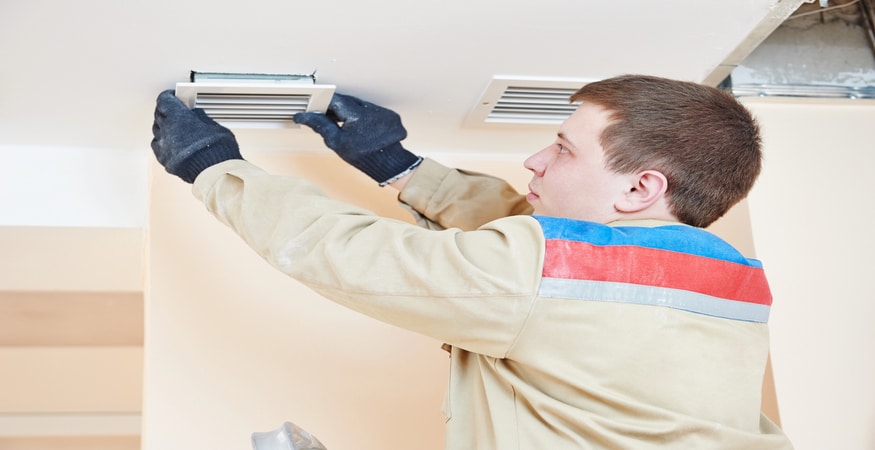 A professional technician wearing gloves installs or adjusts a ceiling air vent cover as part of an air duct cleaning or HVAC maintenance process.