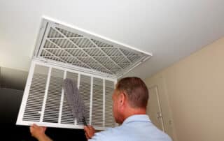 Man cleaning ceiling air vent with duster